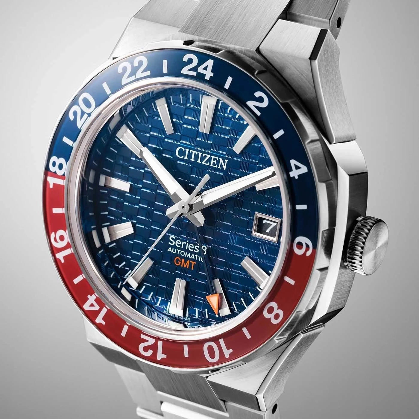 Herrarmbandsur i rostfritt stål i sned vy: blå urtavla, röd/blå GMT-ram och krona