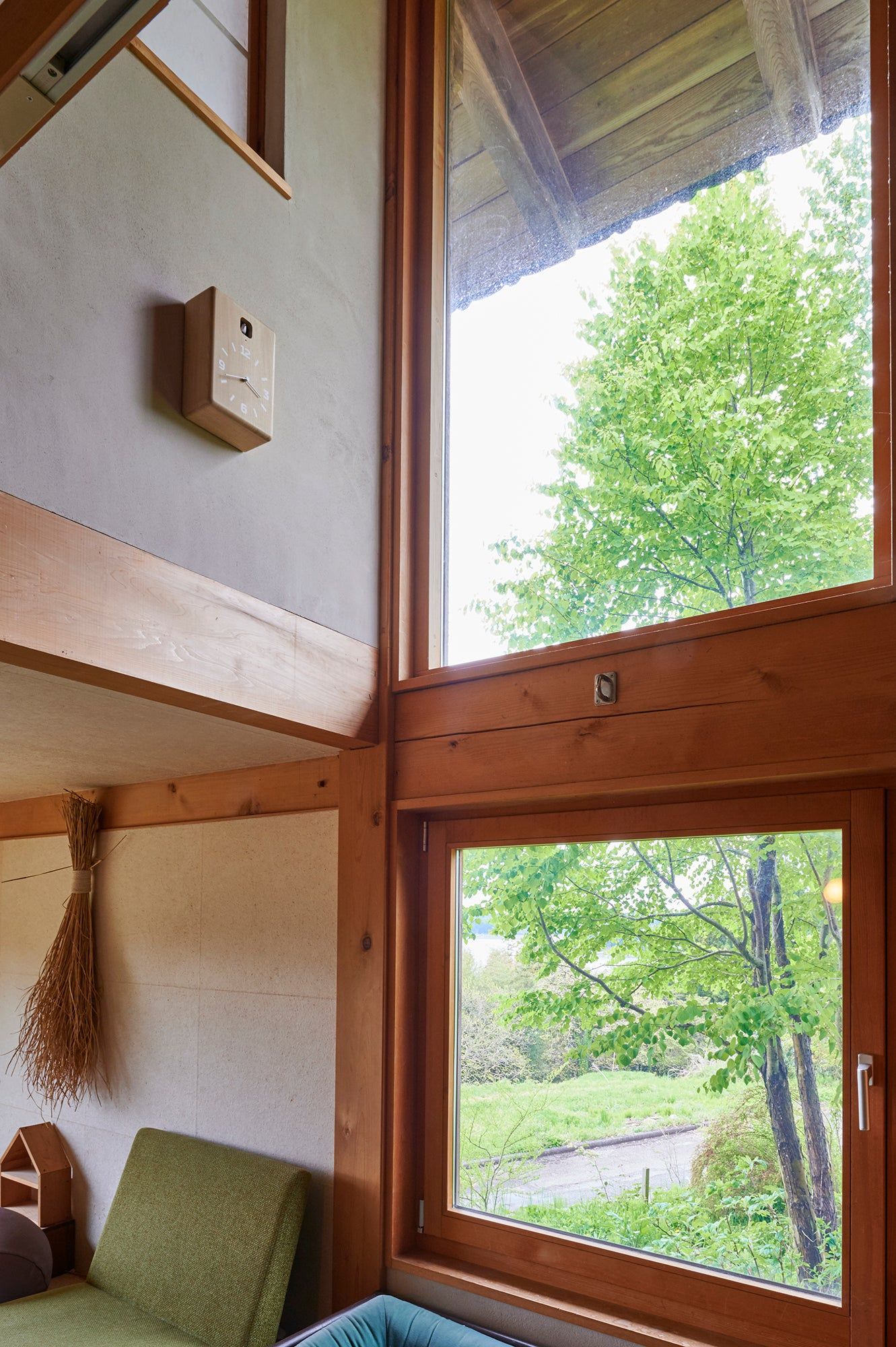Wanduhr an der Wand in Raumecke, neben Fenstern mit Blick ins Grüne