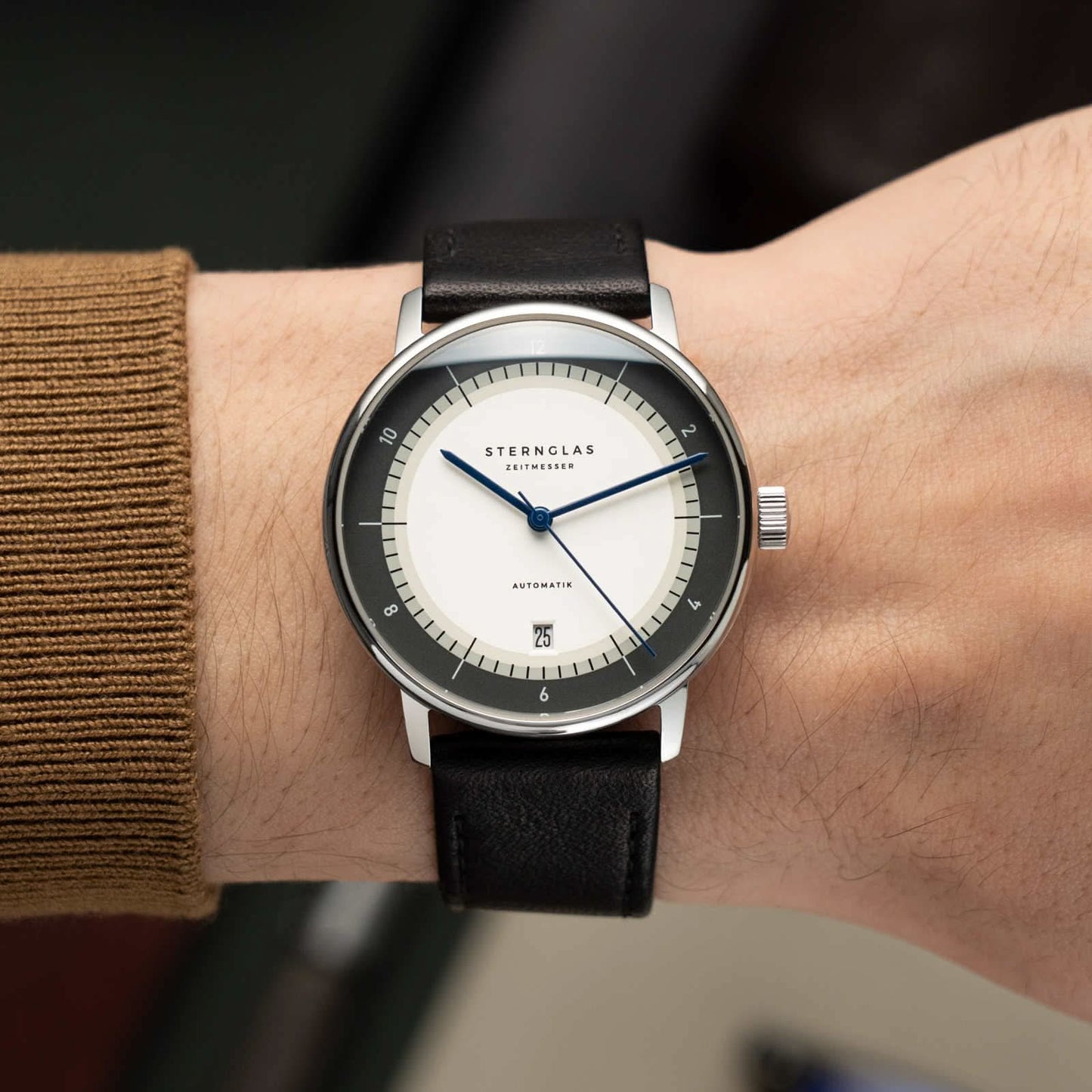 Sternglas herrur med vit urtavla, svart läderarmband på handleden, blå visare