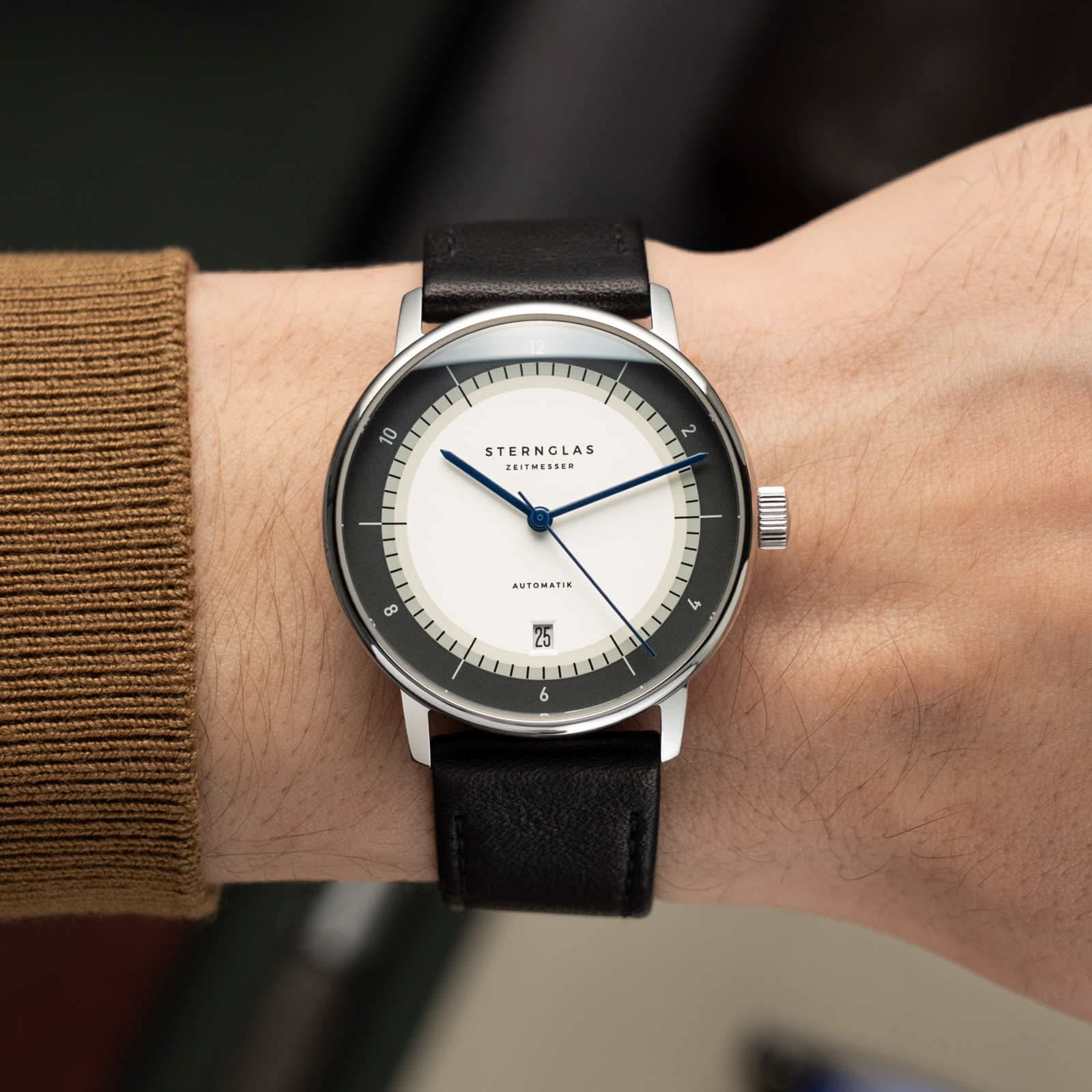 Sternglas herrur med vit urtavla, svart läderarmband på handleden, blå visare