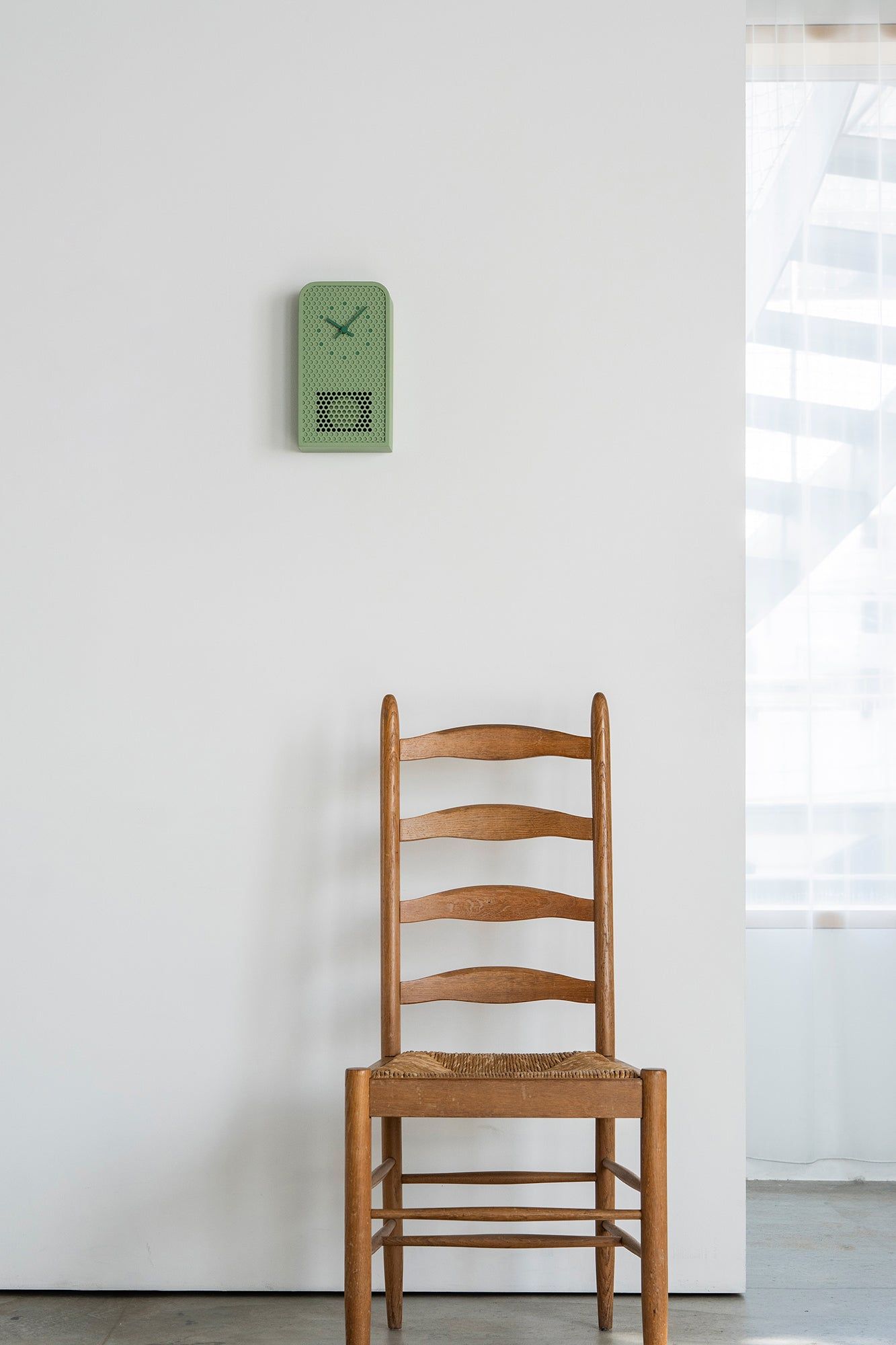 Grüne Metall-Wanduhr mit perforiertem Panel und blauem Zifferblatt, an der Wand