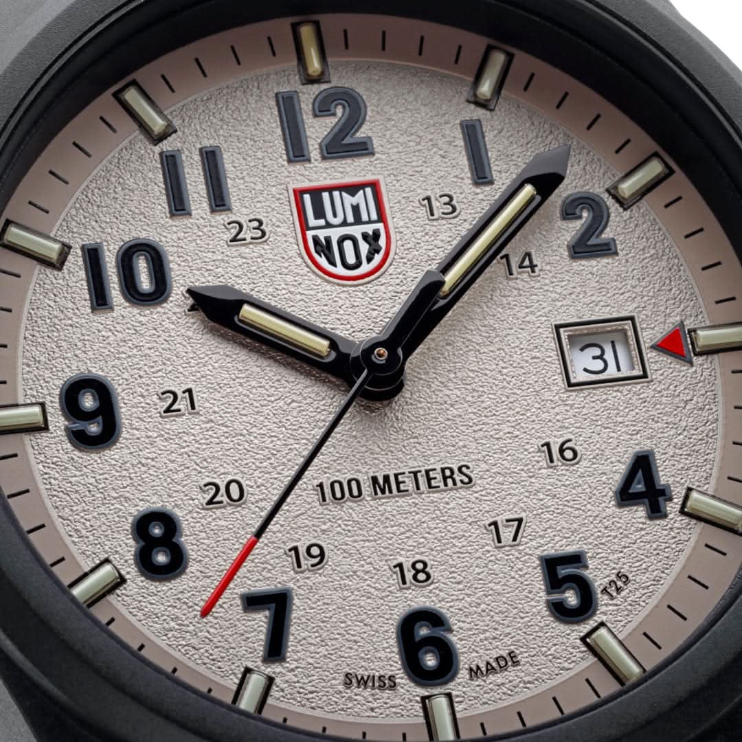 Närbild av urtavla: krämfärgad display, självlysande visare, röd LUMINOX-logotyp och datumfönster.