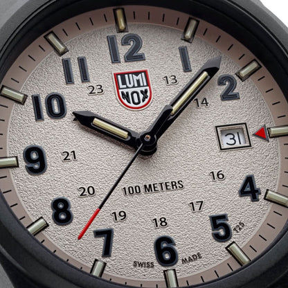 Närbild av urtavla: krämfärgad display, självlysande visare, röd LUMINOX-logotyp och datumfönster.