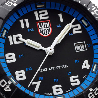 Närbild på urtavla: vita självlysande visare, LUMINOX-logotyp, blå indexskala, datumfönster