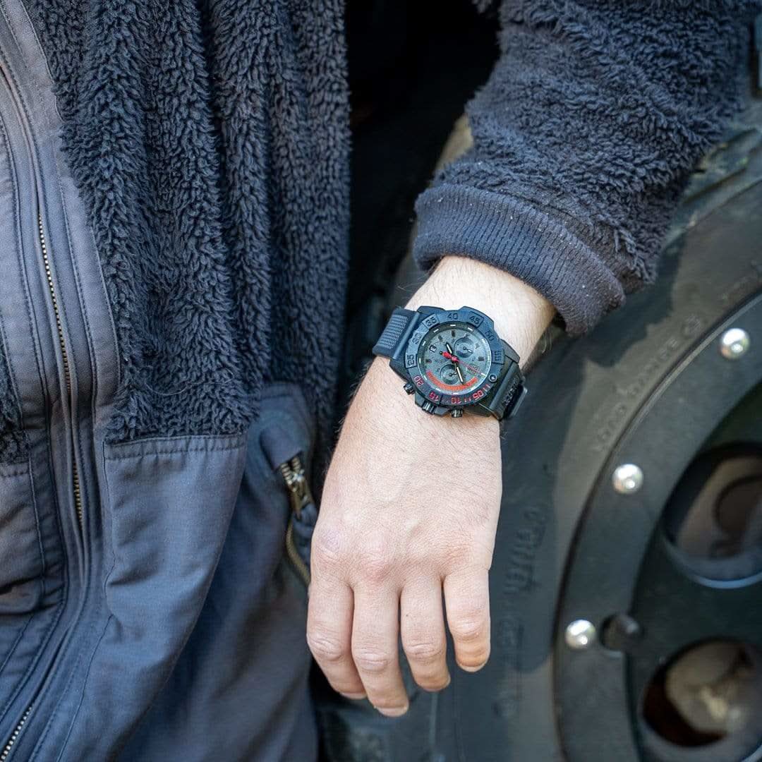 Herrklocka på handleden med svart armband och blå-röd urtavla