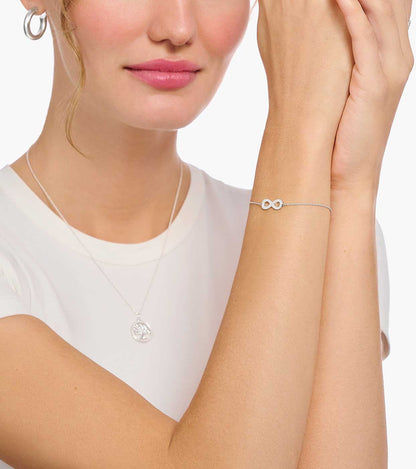 Silverfärgat infinity-armband på handleden med fin länkkedja och litet hänge