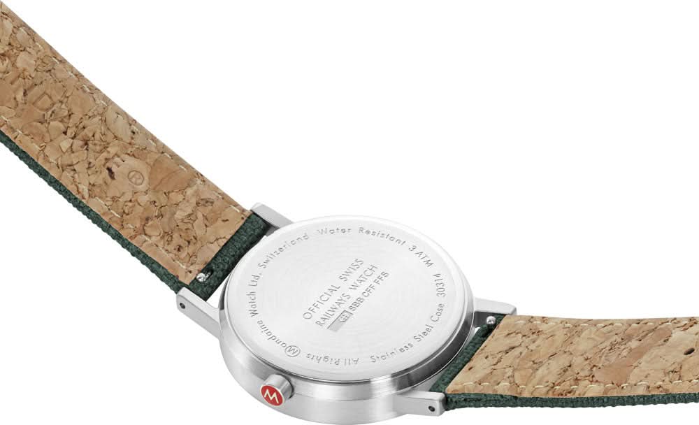 Baksida: silverfärgad klockboett med gravyr och tvåfärgat armband i kork och textil.