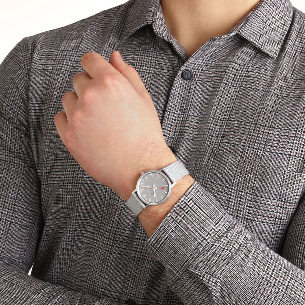 Armbandsur på handleden: grå boett, grå urtavla och grått textilband.