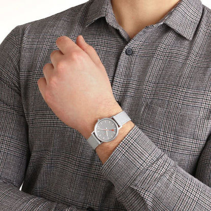 Armbandsur på handleden: grå boett, grå urtavla och grått textilband.