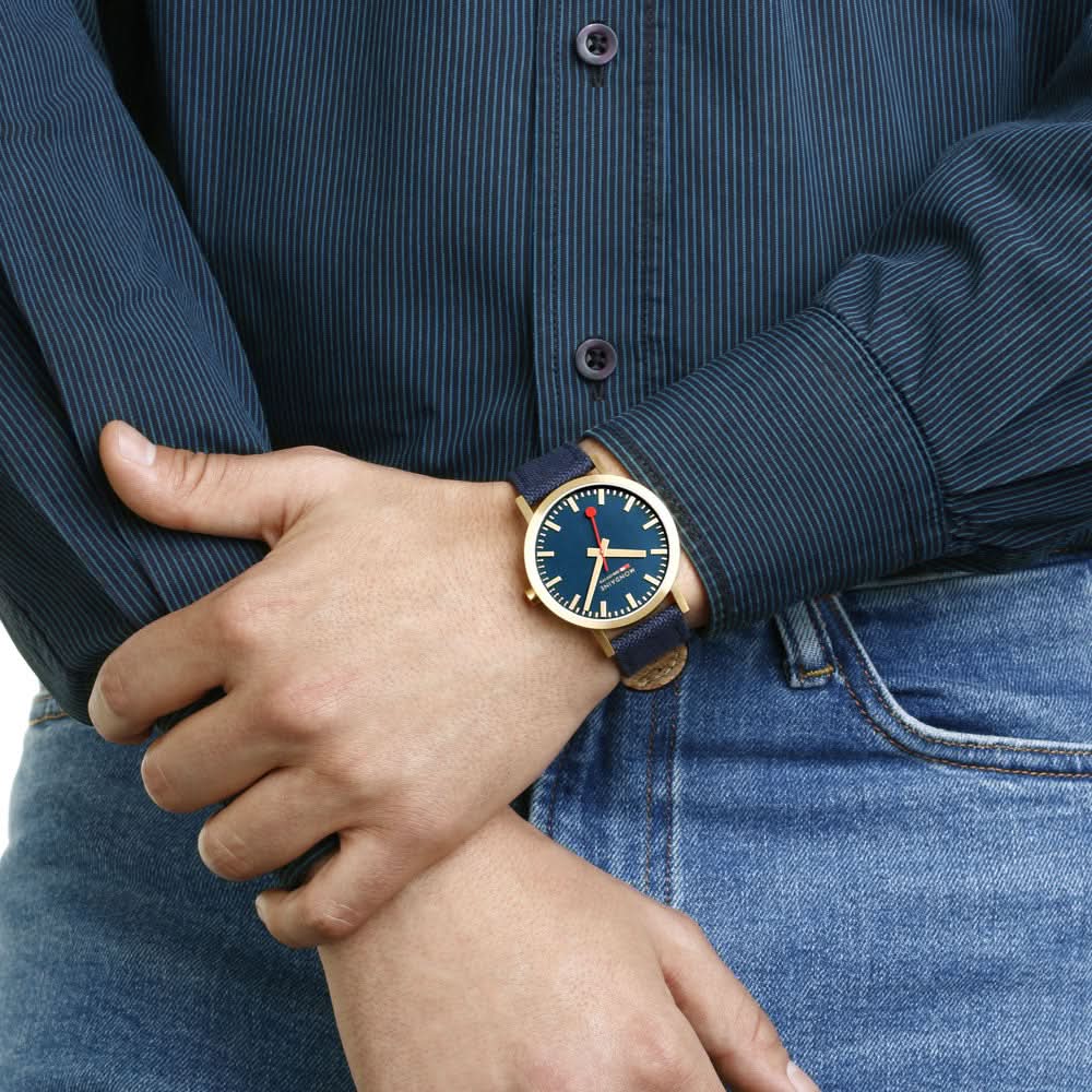 Armbandsur på handleden med blå urtavla, guldfärgad infattning och mörkblått armband
