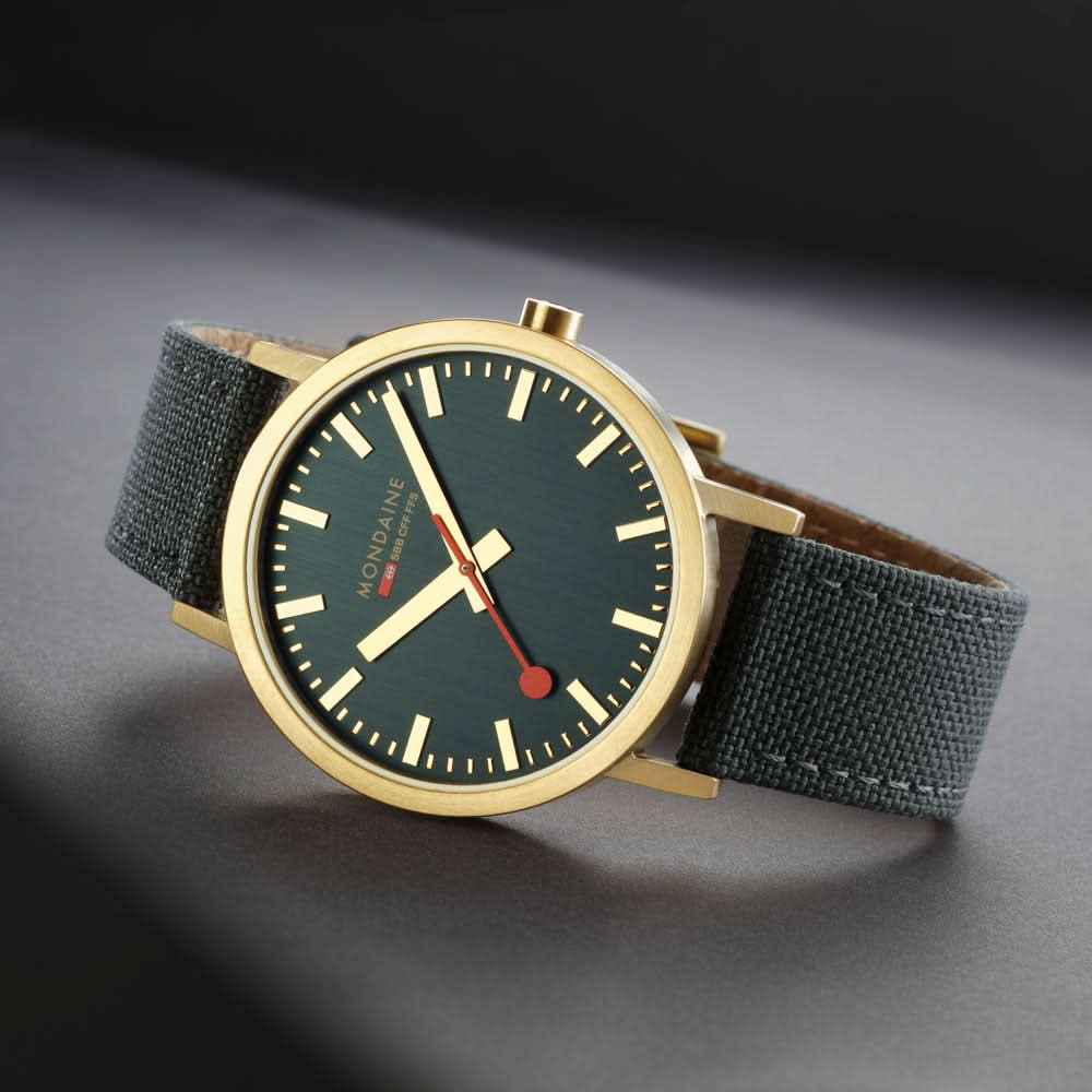 Unisex-armbandsur med mörkgrön urtavla, guldfärgat hölje och grått tygband.