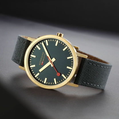 Unisex-armbandsur med mörkgrön urtavla, guldfärgat hölje och grått tygband.