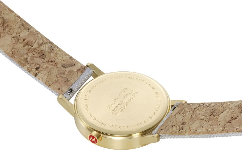 Baksidan av en armbandsur med guldfärgad bottenplatta och brun/beige rem.