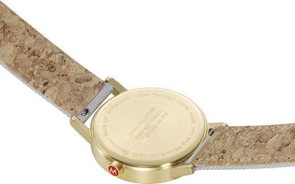 Baksidan av en armbandsur med guldfärgad bottenplatta och brun/beige rem.