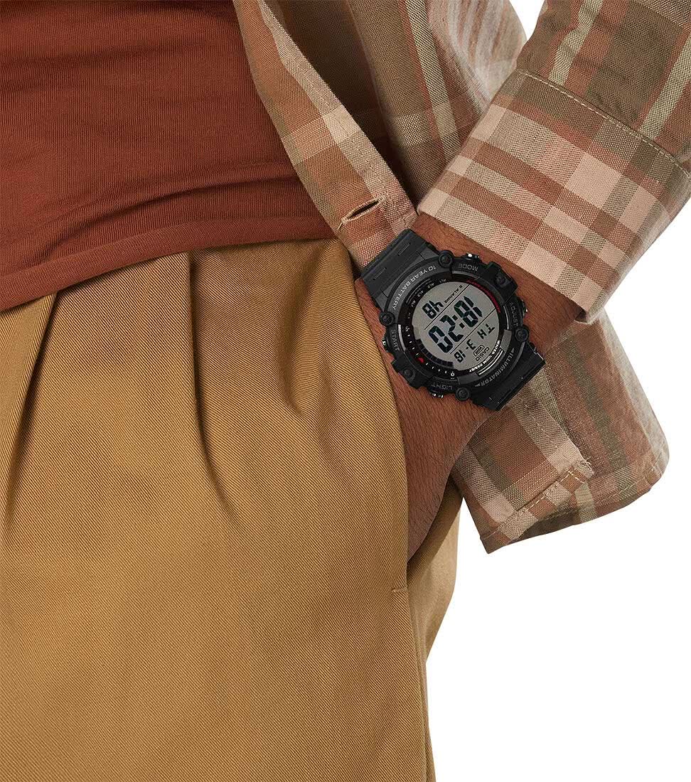 Herrklocka på handleden, svart digital urtavla och gummiarmband, under en rutig skjorta