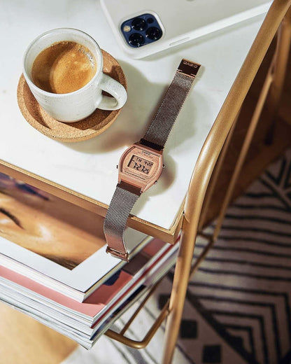 Armbandsur med roséguldigt metallband på en bok, digital LCD-display i detalj.