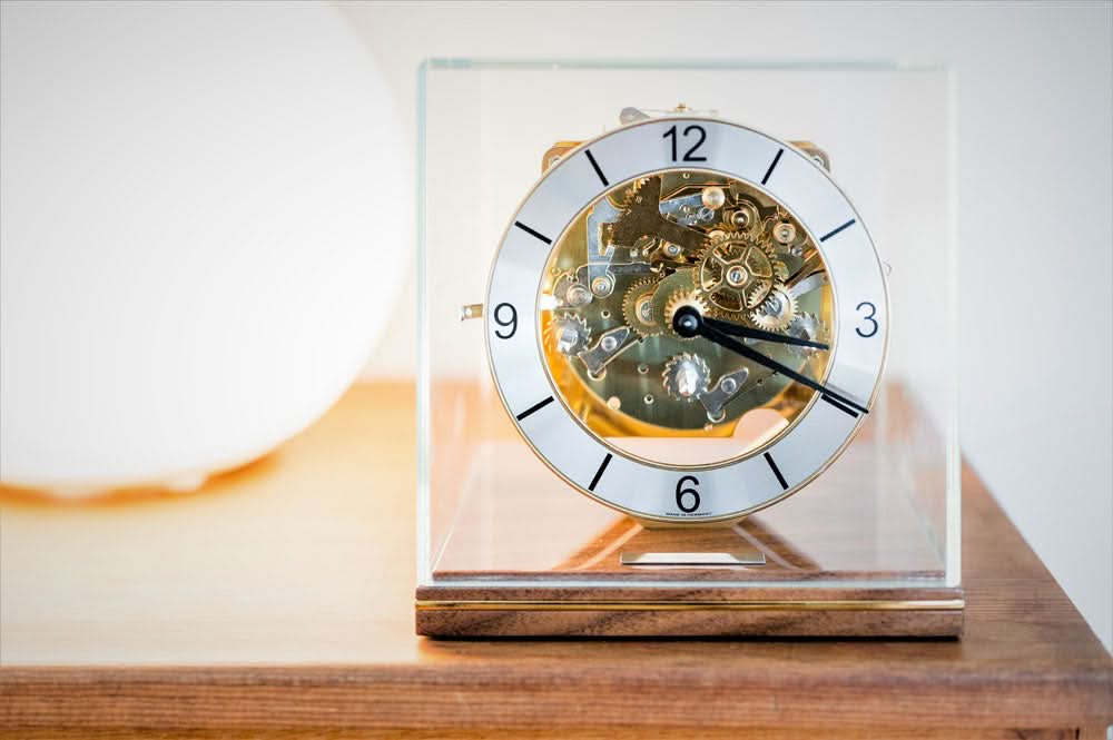Bordsklocka med gyllene urverk bakom glas och rund urtavla, träsockel
