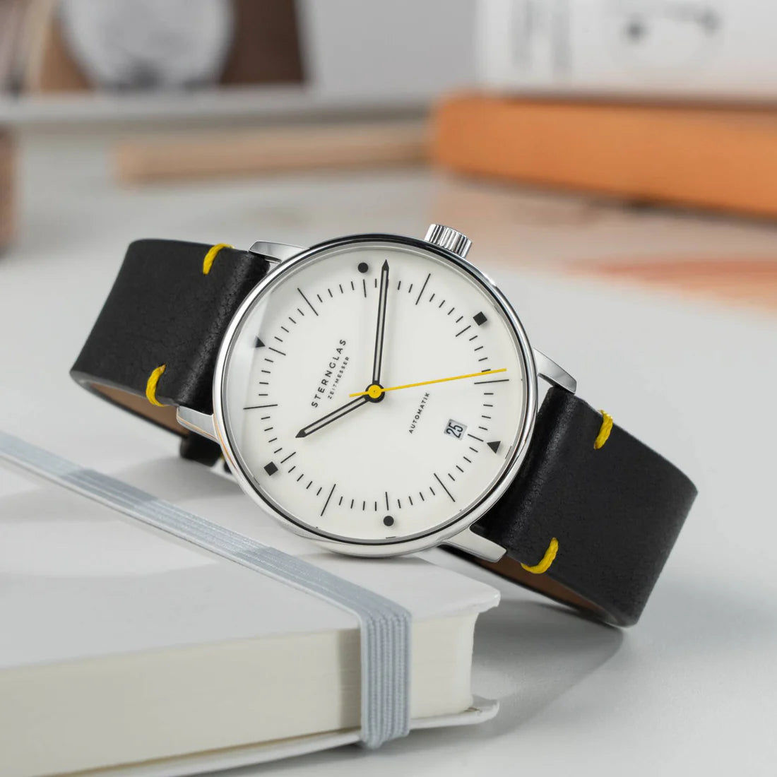 Sternglas Naos armbandsur på bok: vit urtavla, svart läderband med gula sömmar