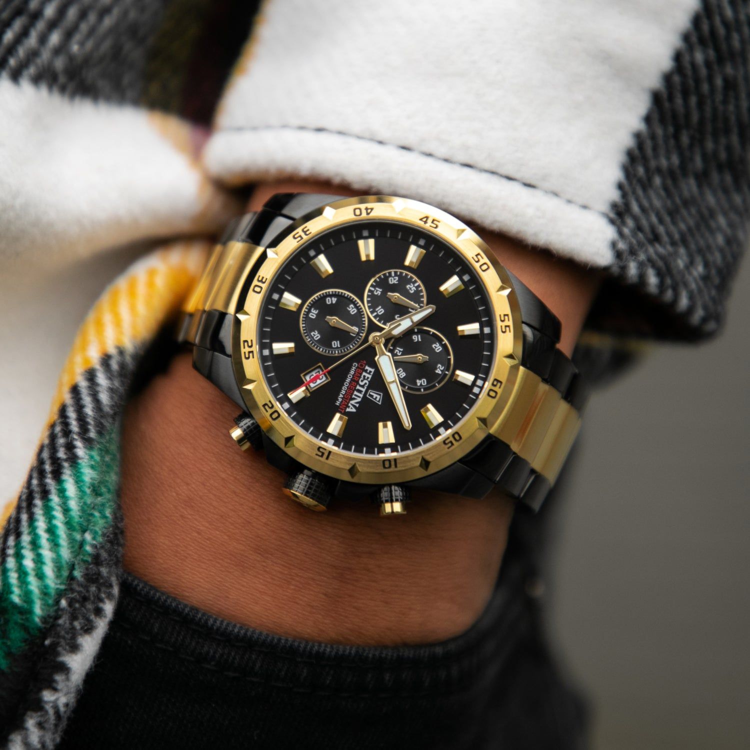 Męski zegarek typu chronograf z czarną tarczą i złotą lunetą na nadgarstku