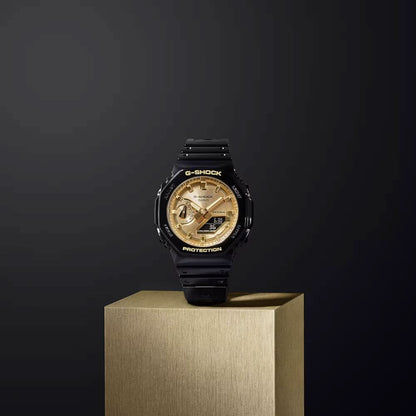 Casio G-Shock herrklocka på piedestal: svart armband och guldfärgad urtavla, runt boett