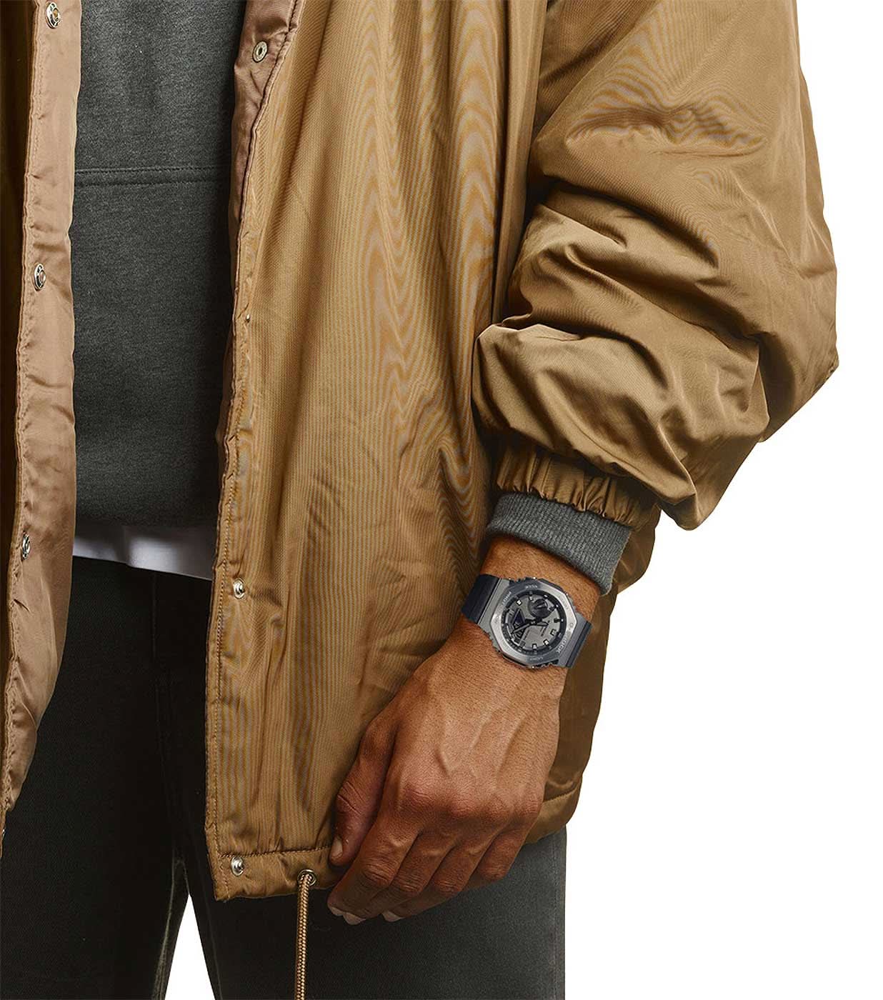 Herrklocka på handleden med svart armband och boett i silver under en jacka.
