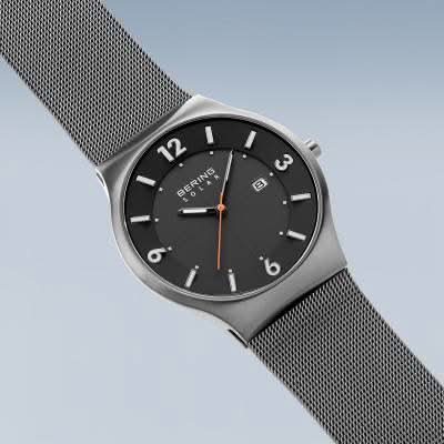 Herrklocka med solcellsdrivning, svart urtavla, orange accenter och mesh-armband i metall