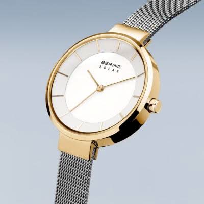 "Damklocka med guldfärgat hölje, vit urtavla och grått metallarmband"
