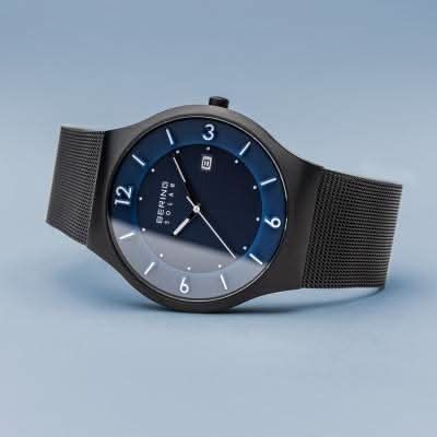 Herrklocka framifrån snett: blå urtavla, svart ram, svart mesh-armband