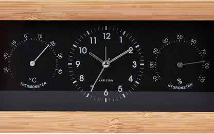 Analog väckarklocka med bamburam i närbild, svart urtavla med temperatur- och fuktskala
