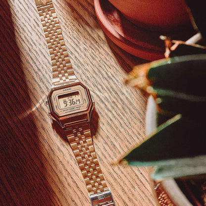 Casio damklocka med metallfärgat metallarmband och digital display på träplatta