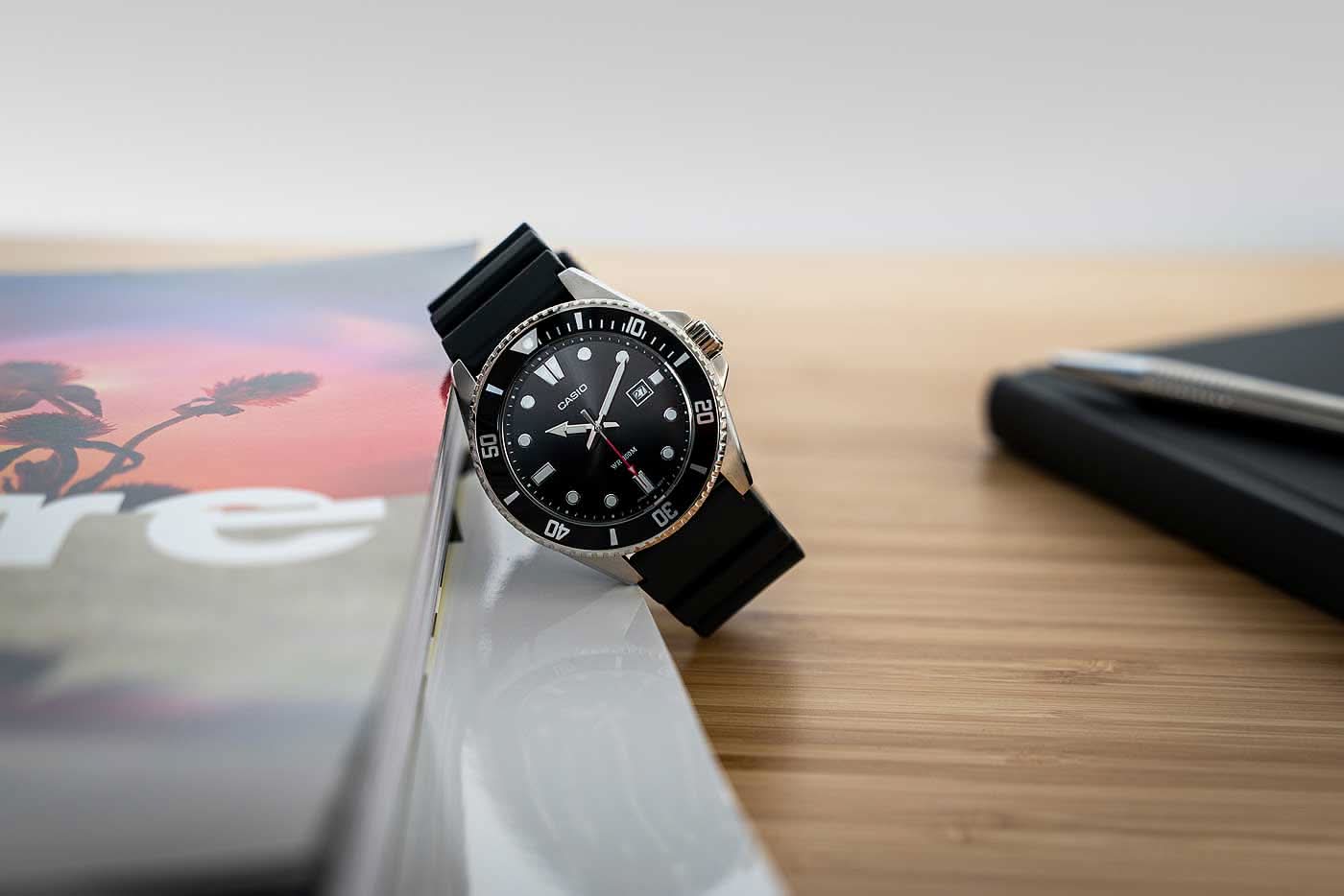Herrdykarklocka med svart urtavla, indexmarkeringar och svart silikonarmband.