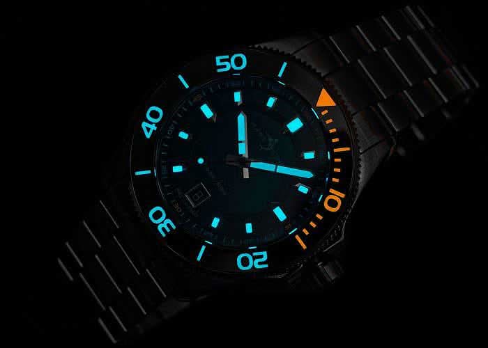 Herrklocka med blå självlysande siffror på svart urtavla, orange bezel.