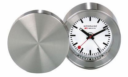 Mondaine reseväckarklocka med öppet silverfärgat lock, runt metallhölje och vit urtavla