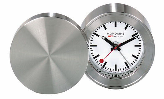 Mondaine reseväckarklocka med öppet silverfärgat lock, runt metallhölje och vit urtavla