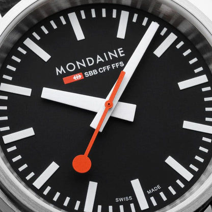Mondaine Stop2Go-klocka närbild: svart urtavla, orange tim- och sekundvisare