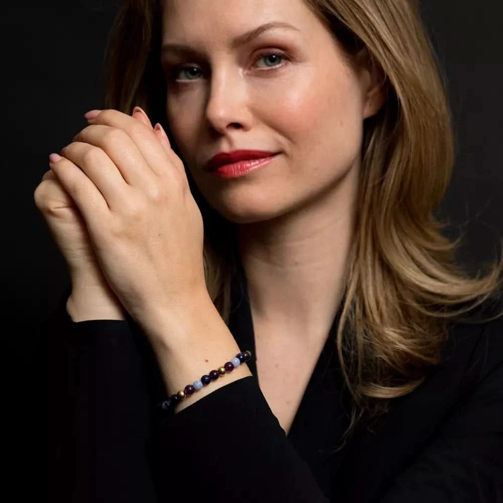 Armband av lila och ljusblå stenpärlor på handleden med guldfärgat lås