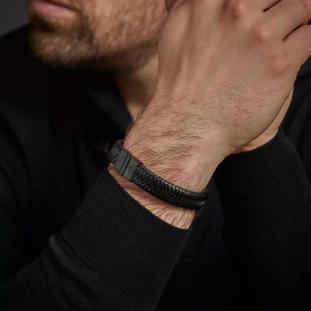 Armband i flätat svart läder runt handleden med lås i rostfritt stål