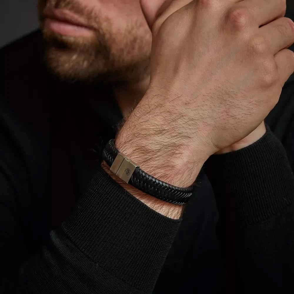 Armband i flätat svart läder runt handleden med lås i rostfritt stål