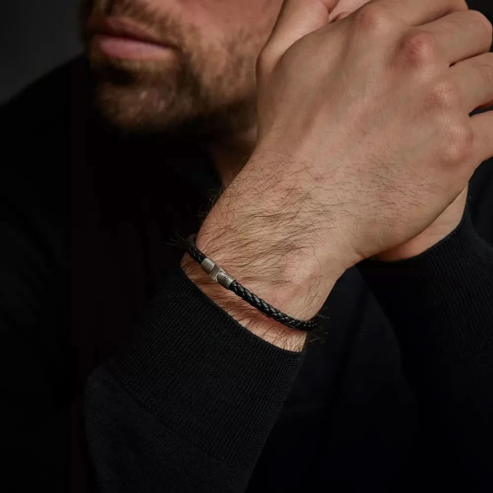 Armband av flätat svart läderband runt handleden med metallspänne