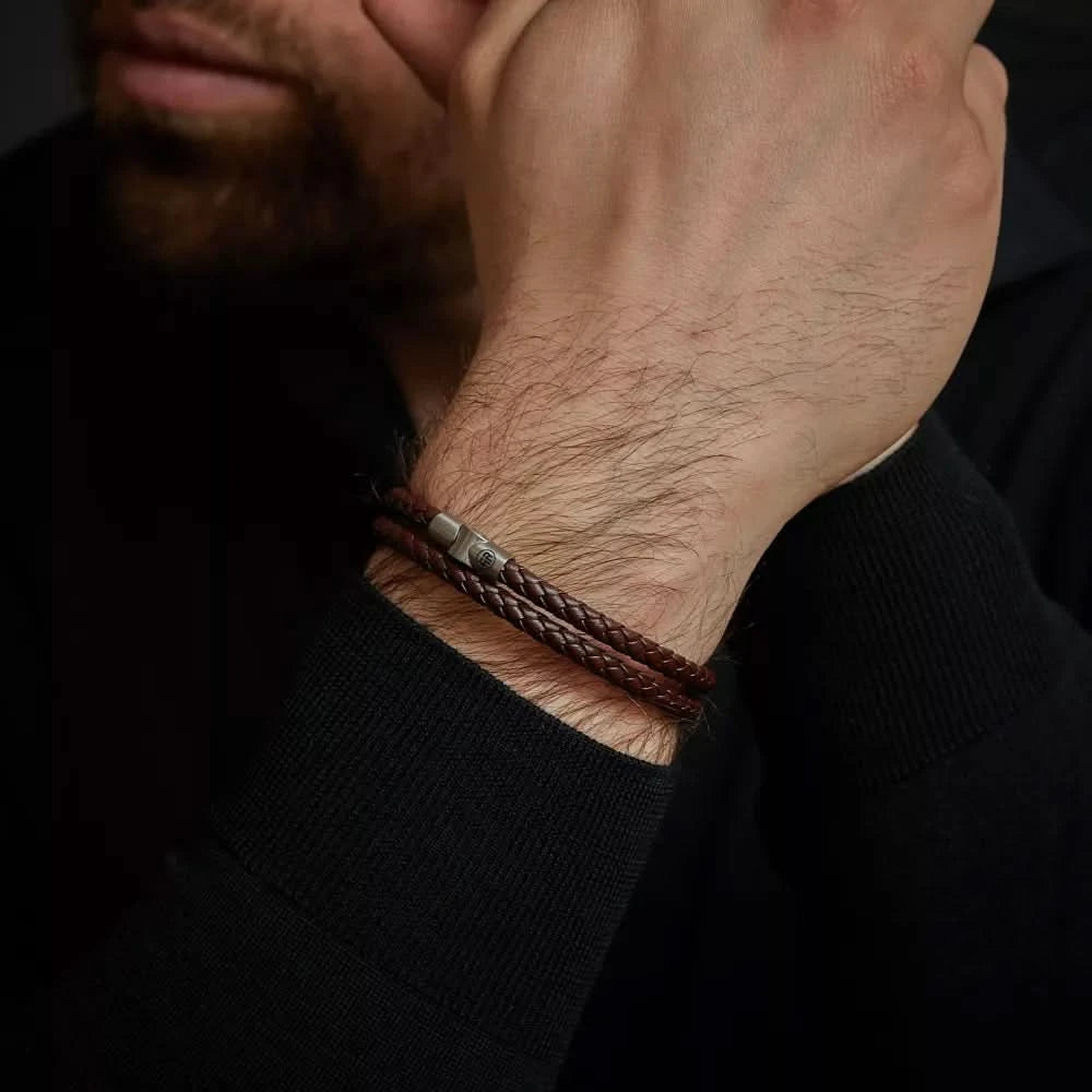 Mörkbrunt läderarmband på handleden, två flätade snören med metallspänne