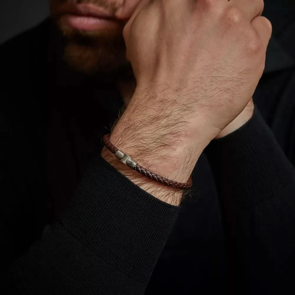 Armband i mörkbrunt flätat läderband runt handleden med lås i rostfritt stål