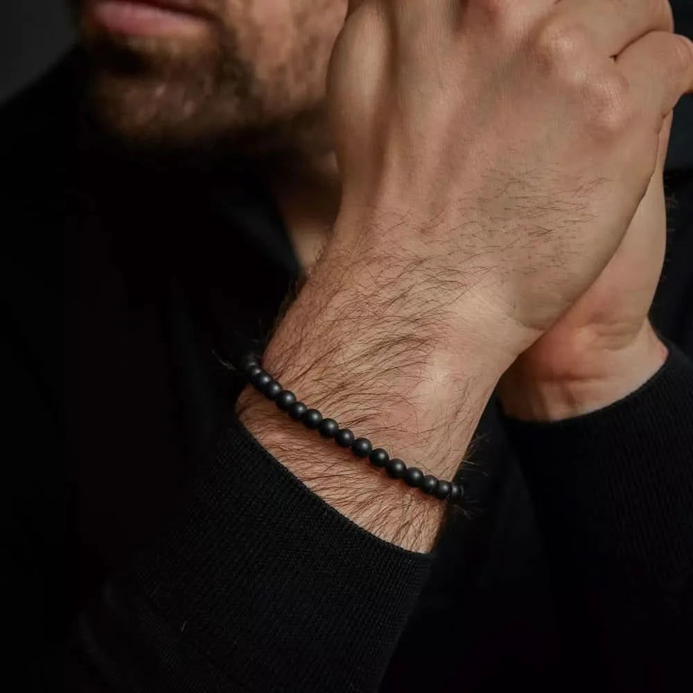 "Armband av svarta naturstenspärlor med svart spänne i rostfritt stål runt handleden"
