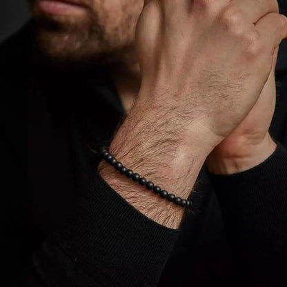 "Armband av svarta naturstenspärlor med svart spänne i rostfritt stål runt handleden"