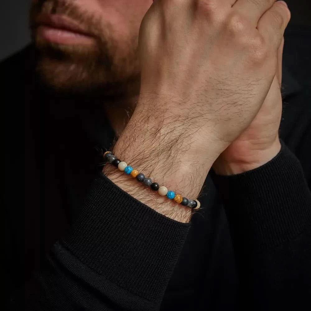"Stenarmband med blå, grå och beige pärlor samt grått spänne i rostfritt stål på handleden"