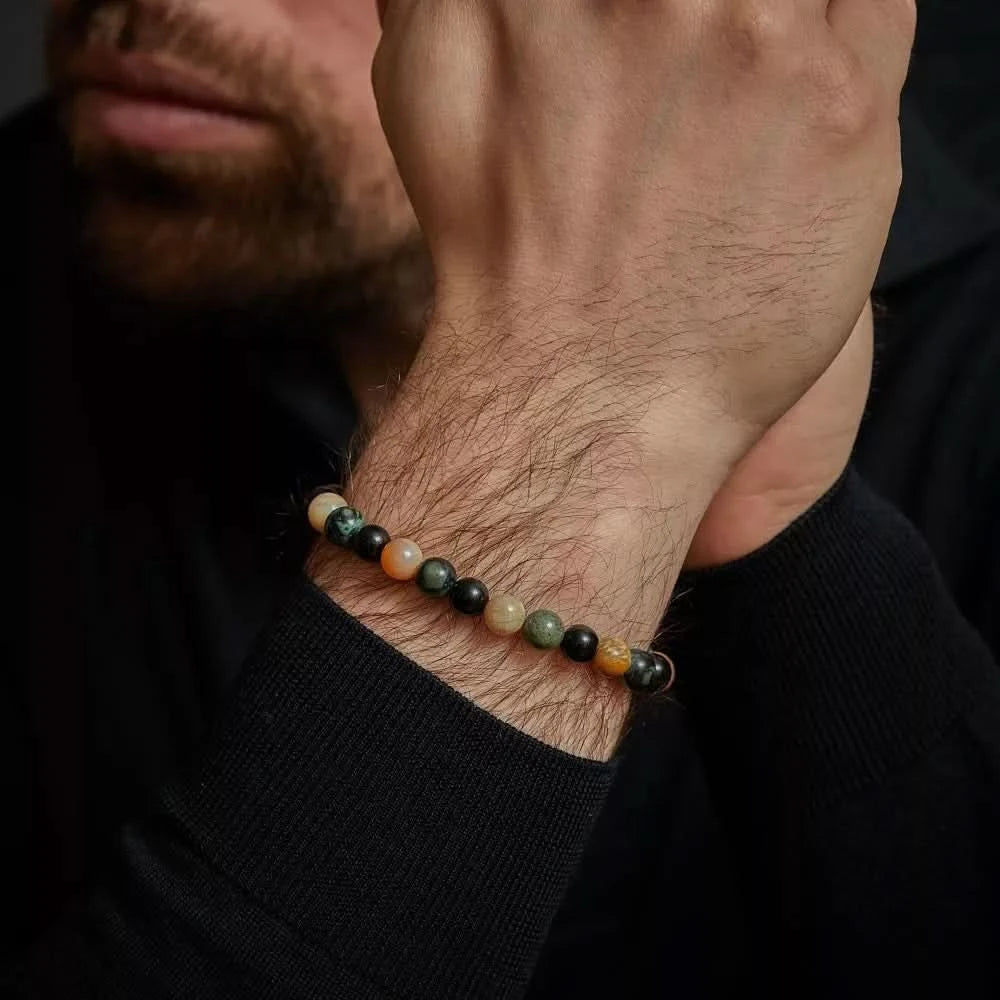 Armband på handleden med mörka och gröna pärlor samt ljusa accenter