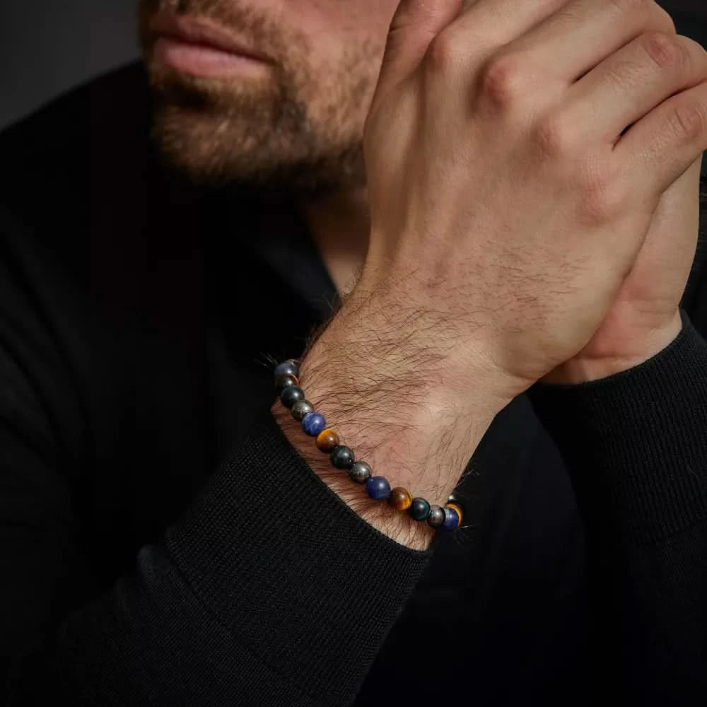 Armband på handleden med blå och gula tigerögon samt grå pärlor och metallås