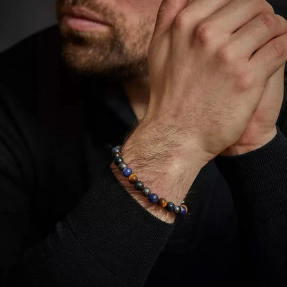 Armband på handleden med blå och gula tigerögon samt grå pärlor och metallås