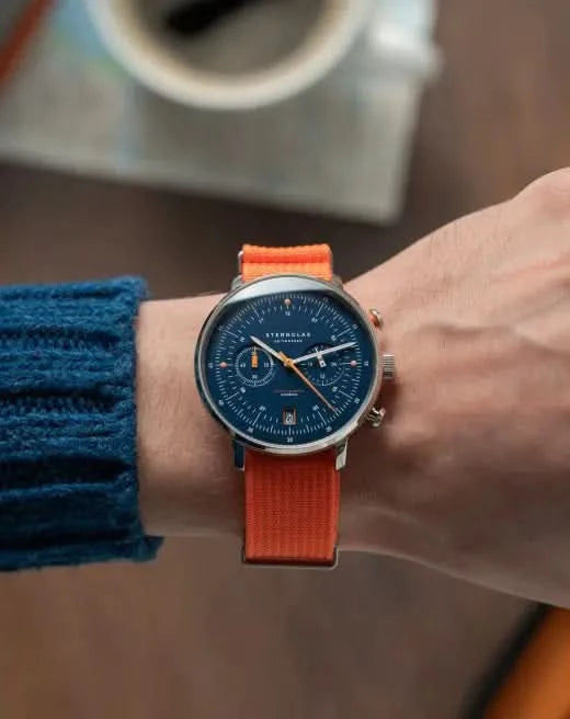 "Sternglas herrur med blå urtavla och orange armband på handleden"