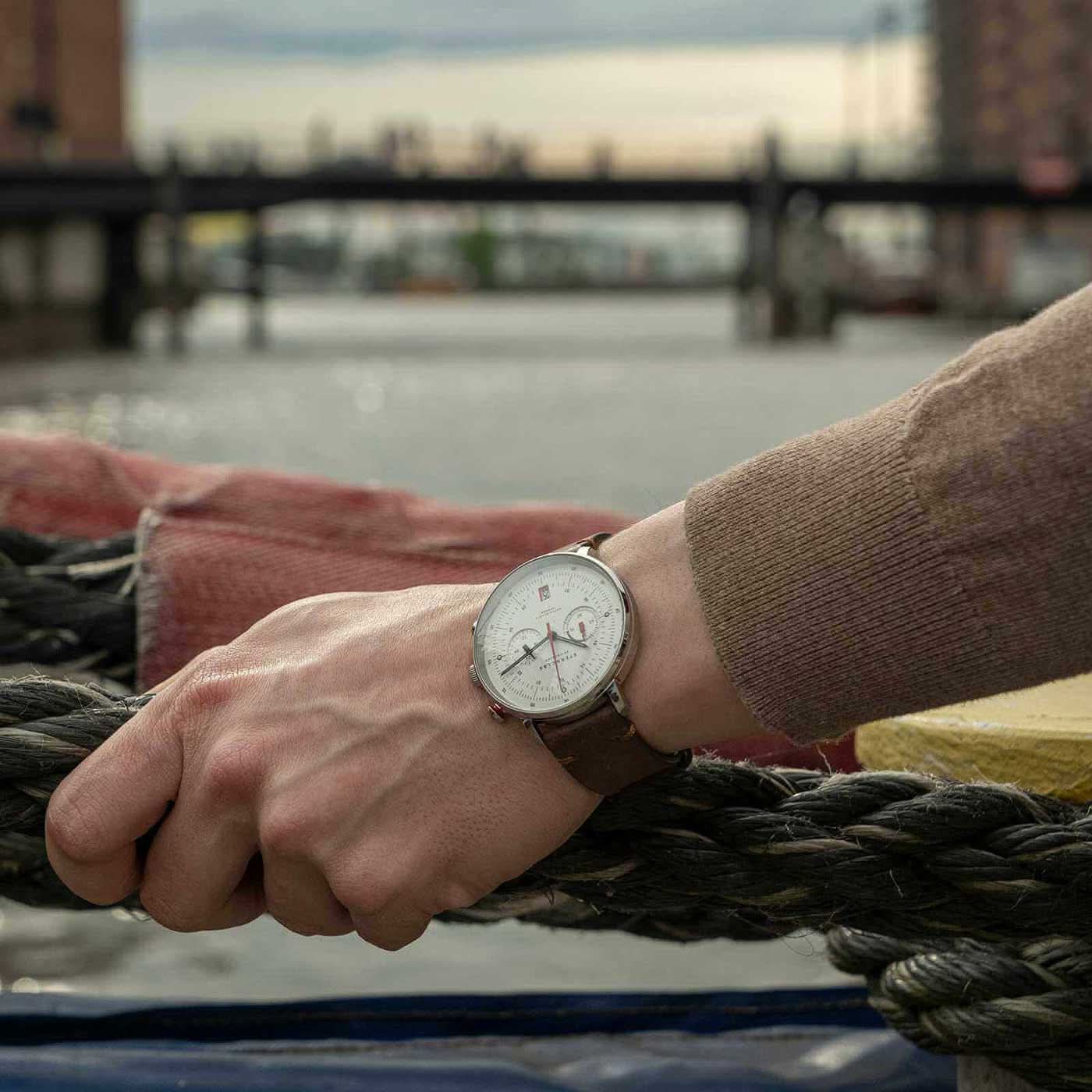 Herrklocka på handleden: brunt läderband, vit urtavla, röda kronografvisare