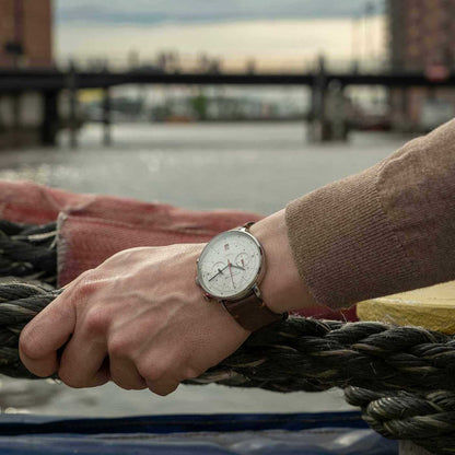 Herrklocka på handleden: brunt läderband, vit urtavla, röda kronografvisare